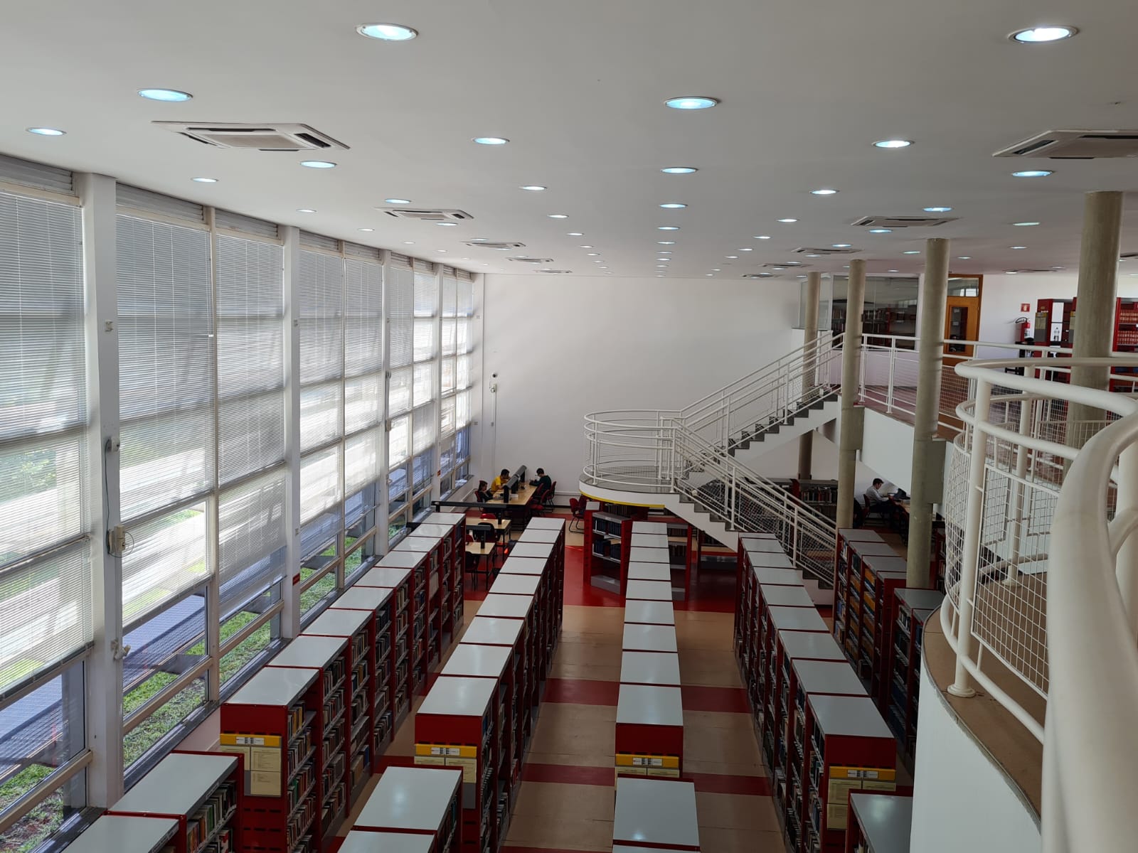 Foto da biblioteca com visão das estantes e escada de acesso.